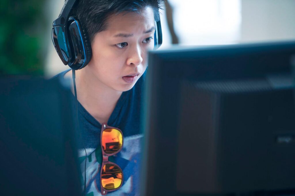 Asiatischer Teilnehmer mit Kopfhörer vor einem PC Bildschirm